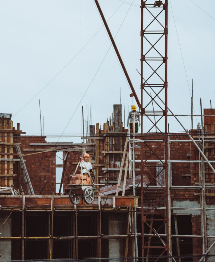 A construction worker on a scaffold at a building site with cranes and brickwork visible.
